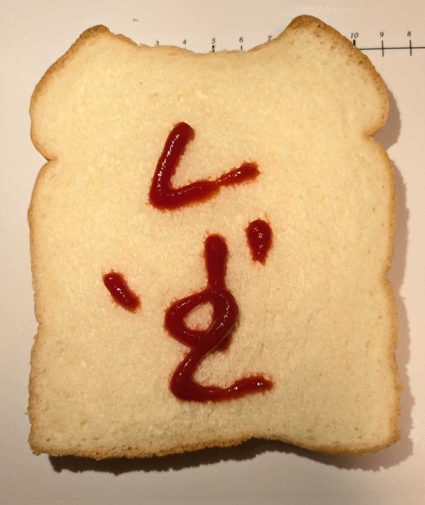 食パンの上にケチャップで漢字の「金」の字が書かれています。