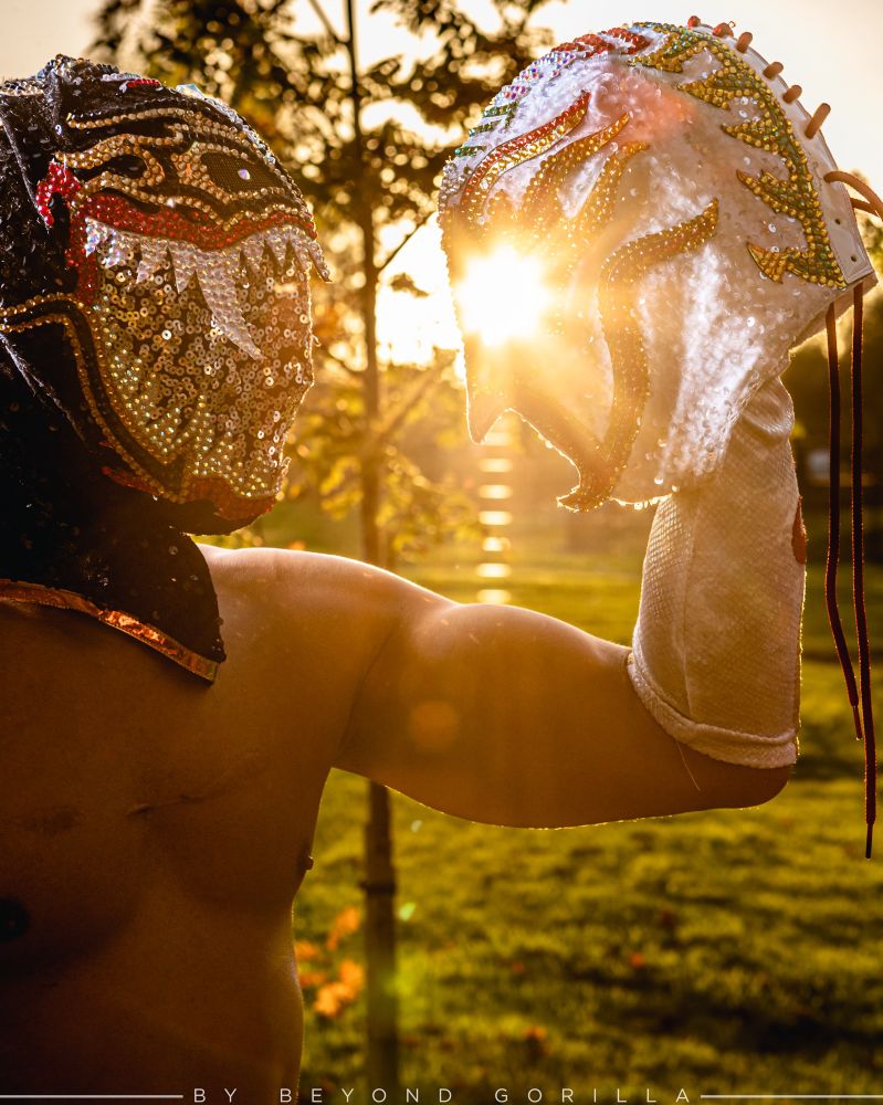 Cmll wrestler Titan holding one of his masks to his head as the sun sets behind him