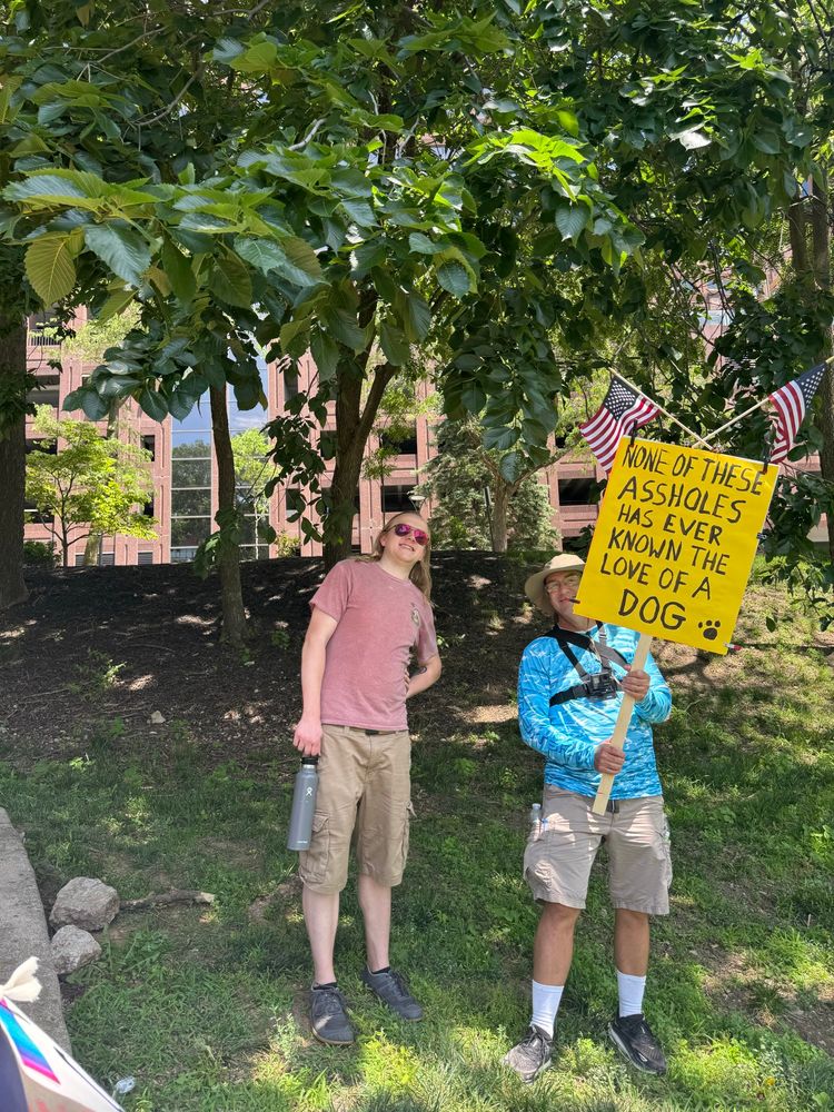 The author of this comment holding a sign reading “none of these assholes has never known the love of a dog.”