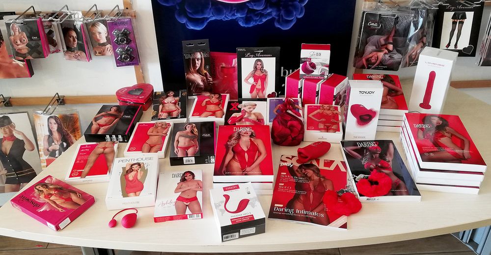 foto del tavolo delle novità con appoggiati prodotti sexy di colore rosso, slip e perizoma, vestitino, set di lingerie, manette, pompette succhiavibrarotanti, ovetti vibranti e petali di rosa.