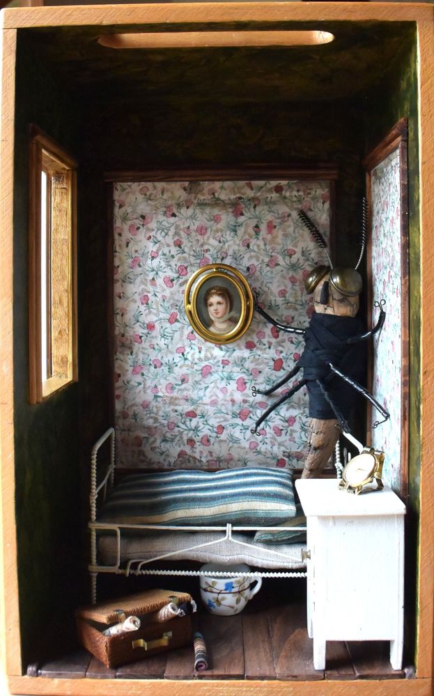 Alle Teile sind realisiert aus Resten und Dingen, die ich noch hatte.
In einem Holzkasten ist links ein Fenster ausgesägt, durch das Licht auf eine altmodische Einrichtung im Stil der Jahrhundertwende um 1900 fällt. Das enge Zimmer wird fast vollständig von einem Bett ausgefüllt, das ein Gestell aus Metall besitzt. Aus der gestreiften Bettwäsche erhebt sich ein überdimensioniertes Insekt aus einem Aststück und Stoff (Körper), Pappe (Rückenschild,Flügel), kleinen Bürsten (Fühler), Messingknöpfen (Augen), Spiralkabelhalter (Beine) und Häkchen (Füße).  Neben dem Bett steht ein weißes Nachttischchen mit einem Wecker (alte Armbanduhr und Heftstreifen aus Metall) darauf, der 7.15 Uhr anzeigt. Vor dem Bett steht der braune Koffer (Streichholzschachtel mit benutztem Stoffteesieb überzogen, Beschläge aus Metall-Heftstreifen) des Handlungsreisenden, aus dem die Stoffmuster hervor ragen. An der geblümten Tapete hängt ein Messing gerahmtes Bild von einer schönen Dame im weißen Chemisekleid des 19. Jahrhunderts.
