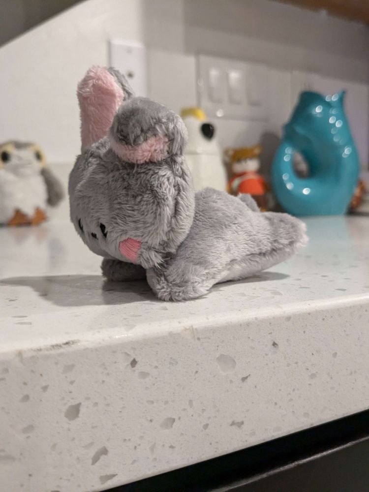 Side view of a gray bunny made with minky fabric. The ears are pink and the face is hand embroidered.