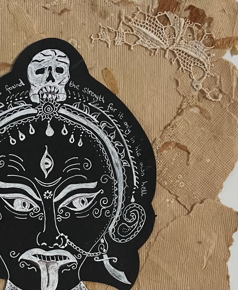 Detail of mixed media collage on tan coloured old, textured, torn paper with vintage lace in the corners, featuring a white drawing on black paper of the fearsome face of the Hindu goddess Kali-Ma.