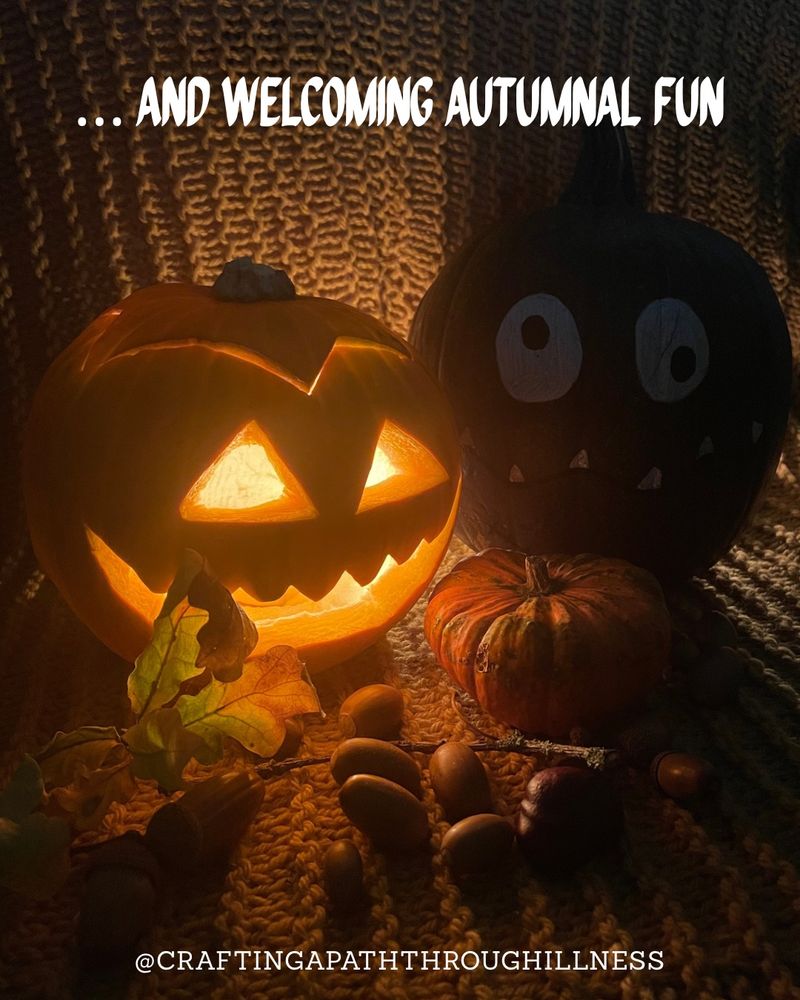 A grinning carved pumpkin is lit from within and sitting in the dark on a textured knitted blanket next to a tiny uncarved pumpkin, acorns, oak leaves, a conker and a green pumpkin painted like a funny version of Frankenstein’s Monster. White text reads: 

.. AND WELCOMING AUTUMNAL FUN

@CRAFTINGAPATHTHROUGHILLNESS