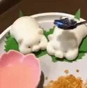 two white pigs are sitting on a white plate with a pink heart shaped bowl .