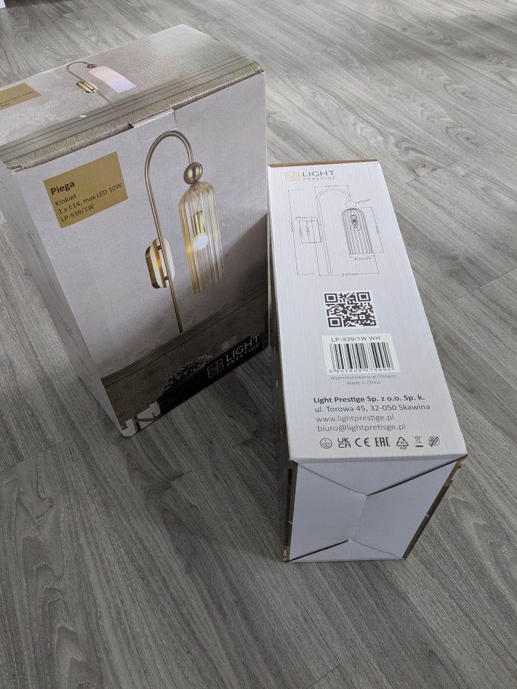 Zwei identischen Verpackungskartons von jeweils einer Wandlampe aus Glas und goldfarbenen Metall. Abgebildet sind die Lampe und eine Zeichnung mit den Maßen