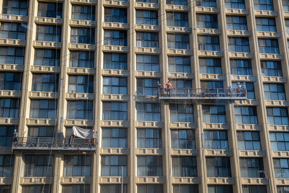 window washers do their jobs on lifts stationed high above the ground, in front of blue windows