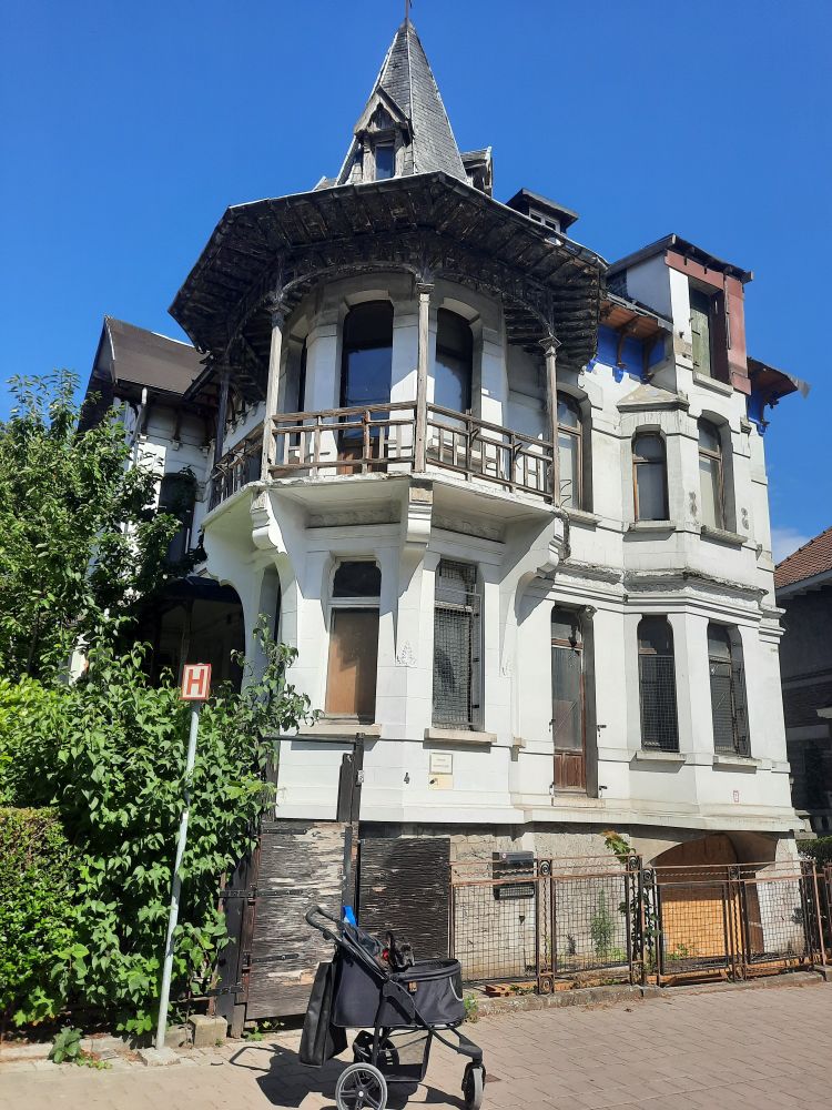 Pax the French bulldog (and hero of the children's book series Mighty Pax's Misadventures) is in his stroller, squinting in the sun while I take this picture. 
Behind him stands a gorgeous beast of a derelict house with tons of tall (and broken) windows, patio that goes around a half tower. It's historically classified, so even though it's housing tons of wildlife, including rats, it can't be torn down. Which is part of the reason I love it :)