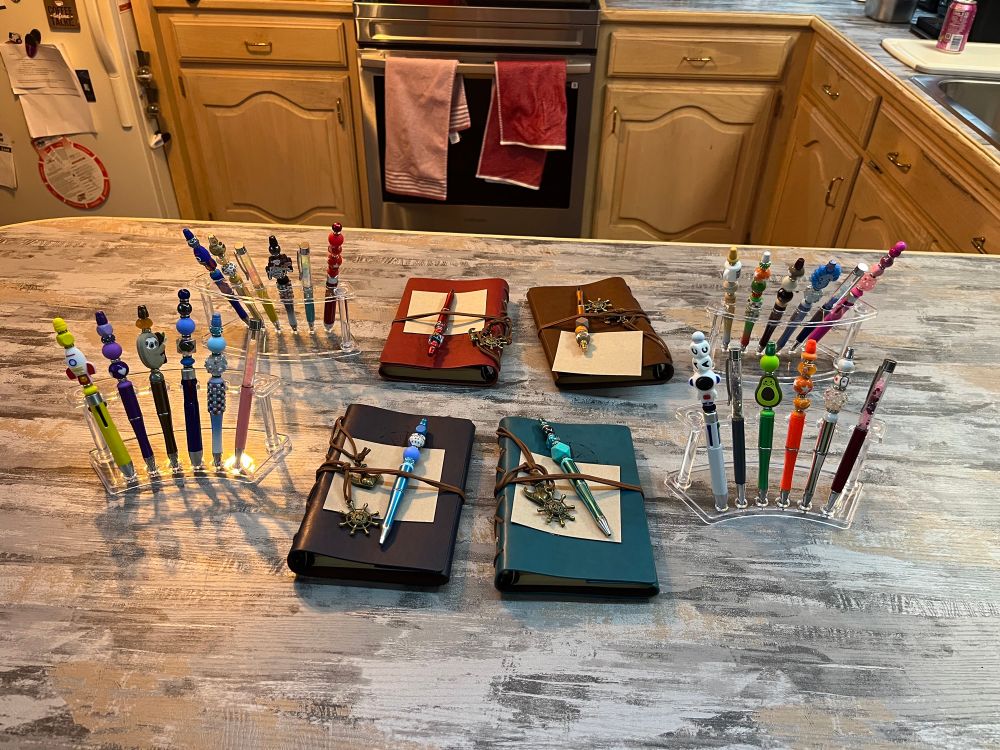 Display of colorful beaded pens and pen/journal sets.
