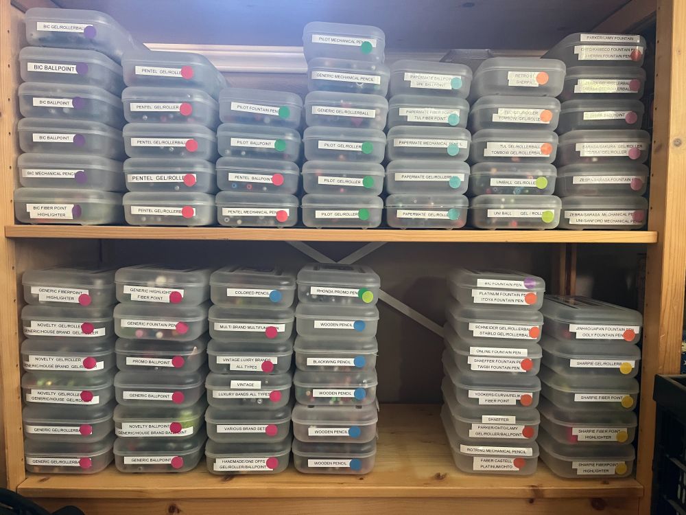 Two shelves of translucent pencil boxes with colored dots and labels of types and brands of pens and pencils.