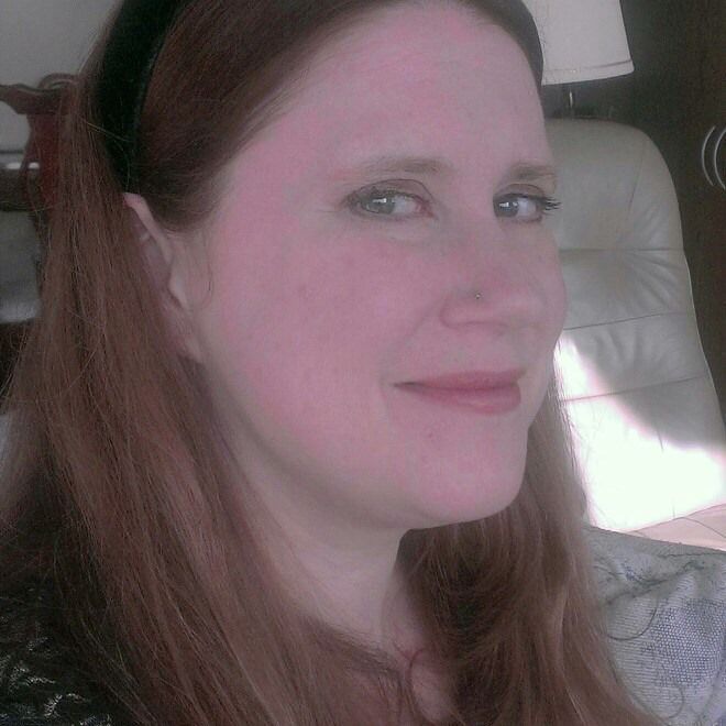 A woman with long red hair is smiling at the camera.