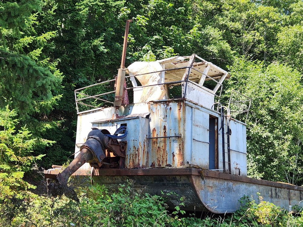 Old oyster barge high and dry on land surrounded by evergreen trees on the side of Linger Long Road by Pacific Seafoods, Quilcene, WA USA  taken July 2025

Plenty of rust, hasn't been used in at least 20 years I would guess...