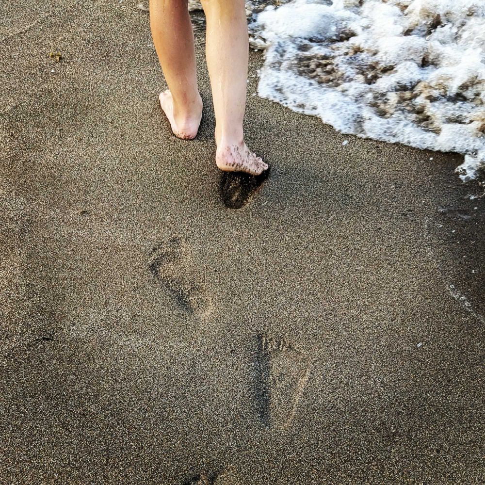 Empreintes de pieds et bas des jambes d'un enfant marchant à la lisière des vagues d'une plage de sable