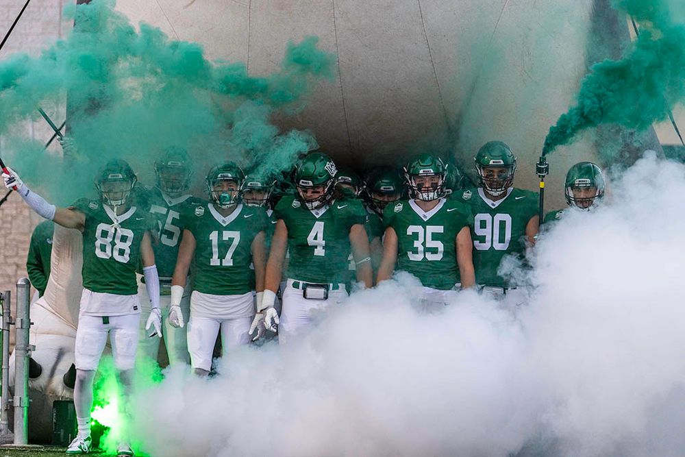 Huskies football players running onto the field through a cloud of green smoke.