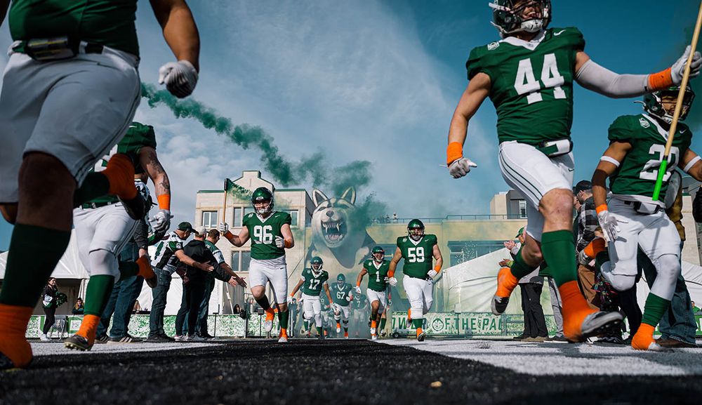 football players exiting the smoke-filled tunnel onto the field during a game.