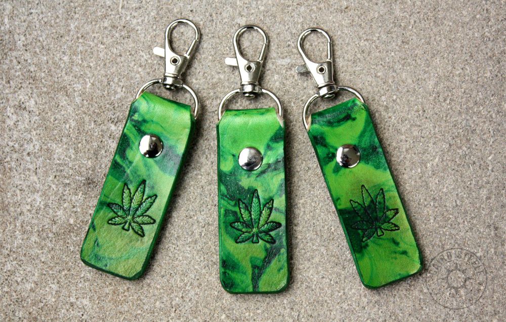 3 leather keychains in green marble, with a hemp leaf stamped on the front. Each has a silver colored clip and matching rivet.