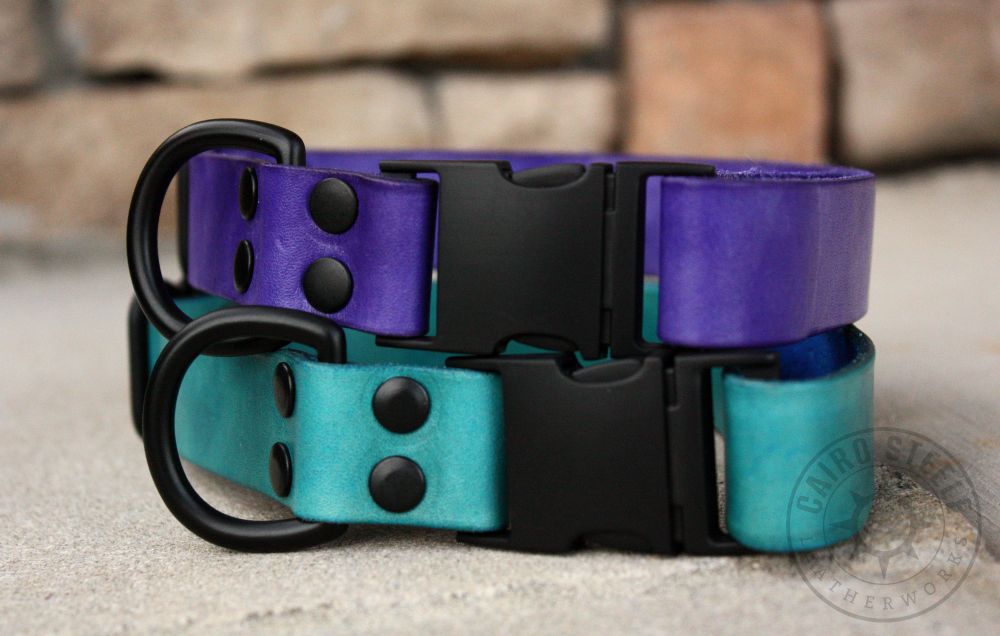 Two leather collars stacked on top of each other. The top is violet with black hardware, and the bottom is aqua with black hardware. Both have a side-release buckle, D-ring, and adjustable slider