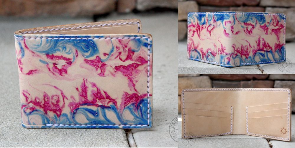 A handmade leather wallet. The shell of the wallet is natural beige with blue and pink marbled stripes resembling a trans flag. The interior of the wallet is solid natural beige with a makers mark in the bottom right corner. The wallet has white stitching around the edges.