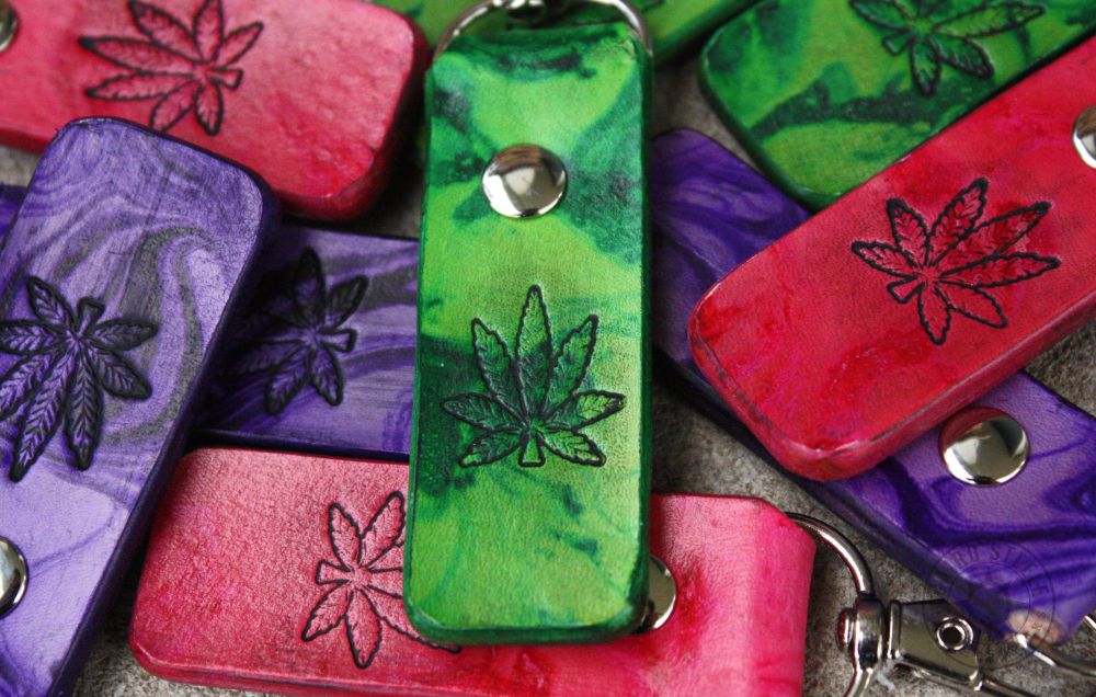 A pile of marbled leather keychains in green, purple, and pink. Each has a hemp leaf stamped on the front