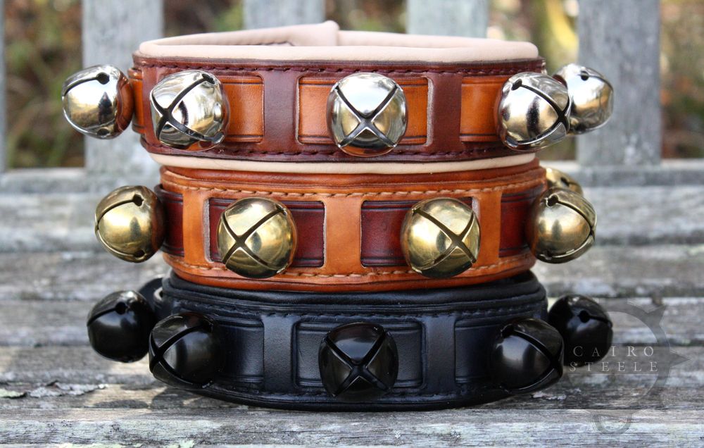 3 leather collars with sleigh bells stacked on top of each other. The top is brown with silver bells, the middle is brown with brass bells, and the bottom is solid black with black bells.