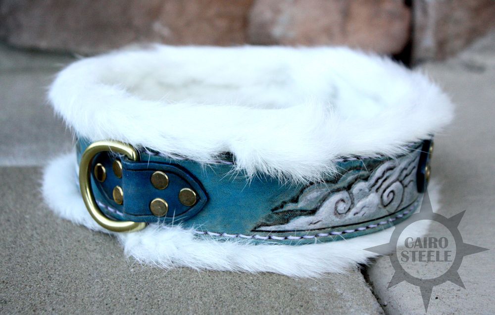 A handmade leather collar. It has a light blue base strap with hand tooled and painted clouds, a darker blue top strap with antique brass hardware, a white rabbit fur liner, and white stitching