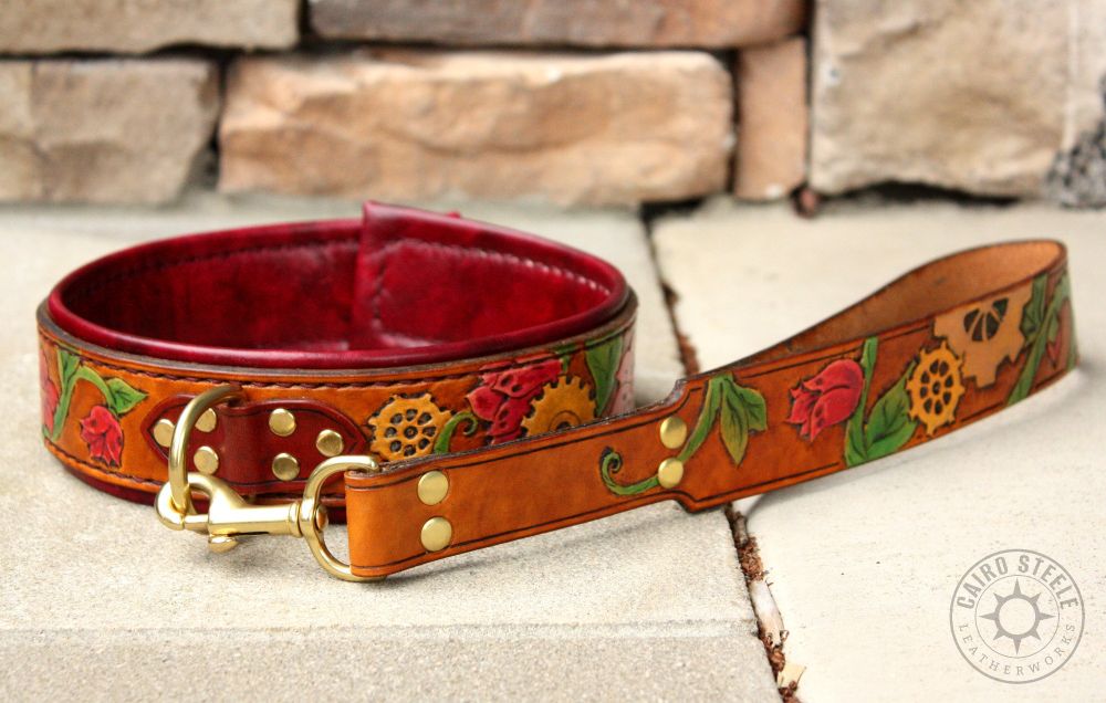 A handmade leather collar and matching short leash. The base straps are golden brown and tooled with vines, flowers, and gears across the entire body of both collar and leash. The vines are painted green with red flowers, and the gears are various shades of metallic gold. The collar has dark brown top straps with brass hardware and a dark red liner.