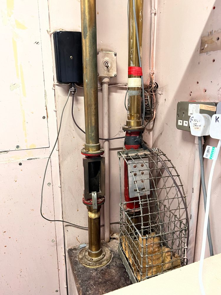 When the operators got a call about a fault they'd scribble it down on a docket and pop it in a little shuttle thing and then it would go into this air tube system which emerged next to the test desk. The basket is to stop them flying all over the place. Supermarkets use a similar thing now for sending cash from the tills to the back of the shop.