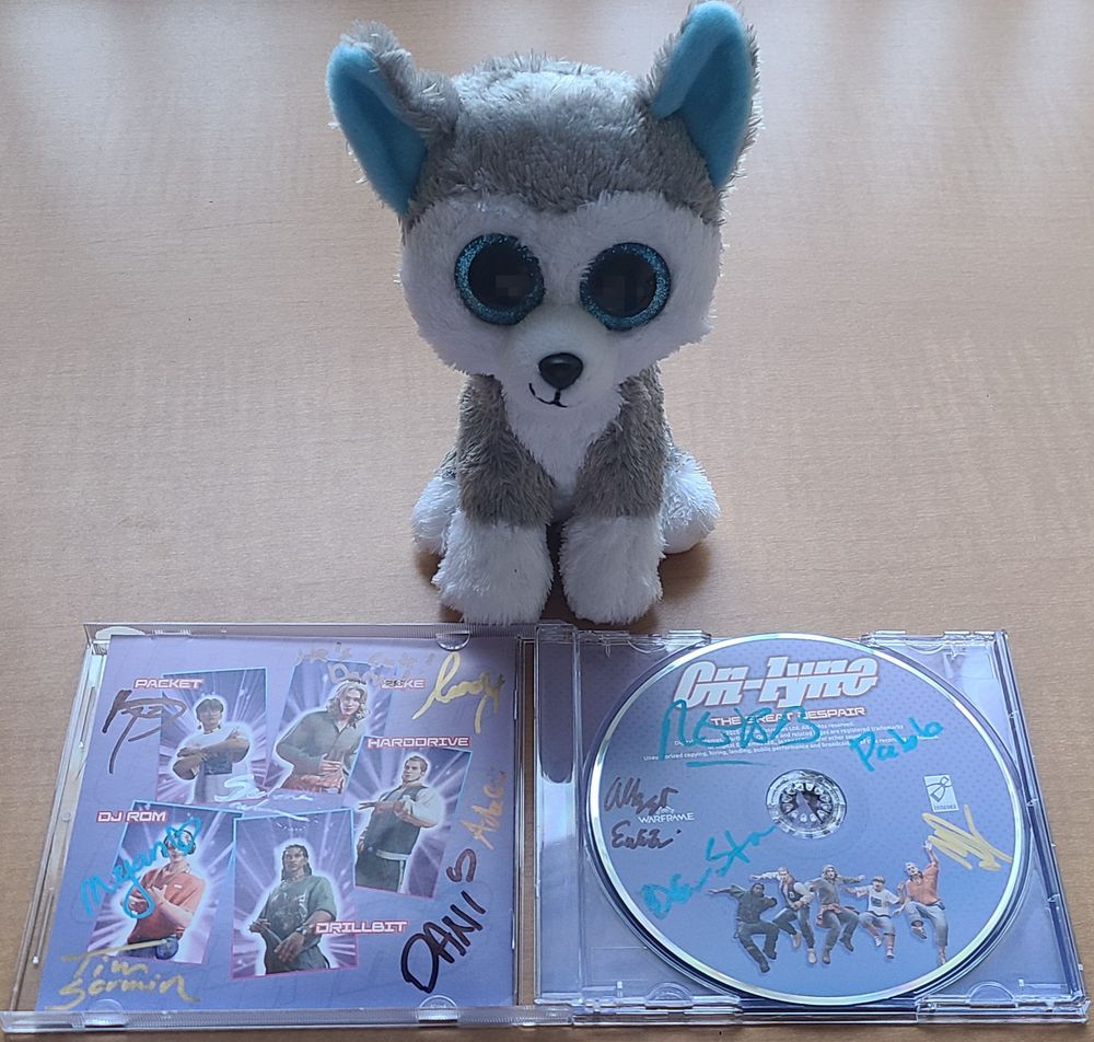 An image of a plush husky looming over a CD copy of On-Lyne's 'The Great Despair", signed by a myriad of members from the warframe team.