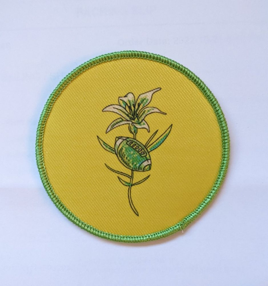 A circular/roundel sew-on patch depicting a Canadian Football League football in-front of a Prairie Lily on patch of Saskatchewan's gold and green colours