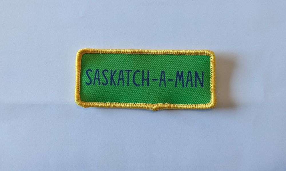 A rectangular sew-on patch depicting the logo for Canadiana comedy comic book, Saskatchewan, on the patch of Saskatchewan's gold and green colours