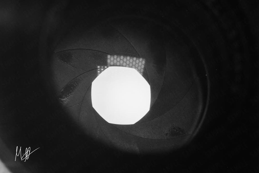 A darkly contrasted macro photograph of the aperture blades of a vintage camera lens