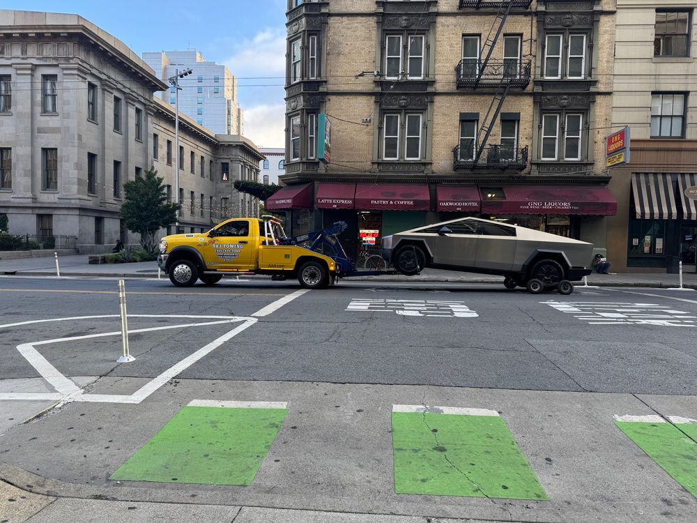 A tow truck pulls a sad tesla cybertruck down the street. How embarrassing.
