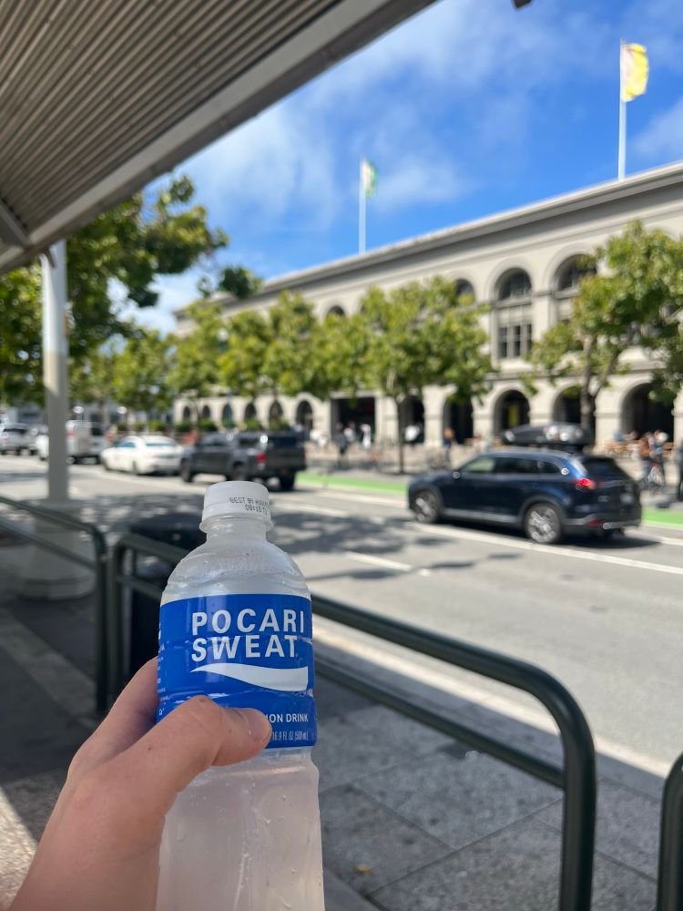 Hand holding a bottle of Pocari Sweat with the San Francisco Ferry Building in the background 