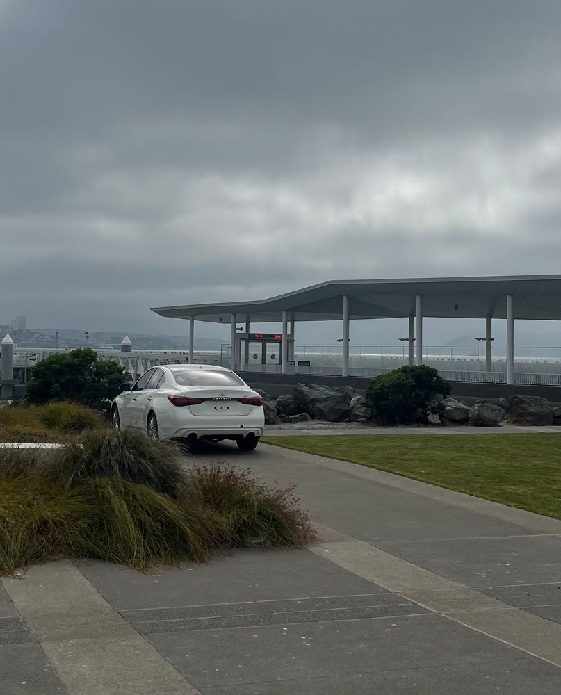 White sedan with no rear license plate parked on sidewalk in front of ferry terminal
