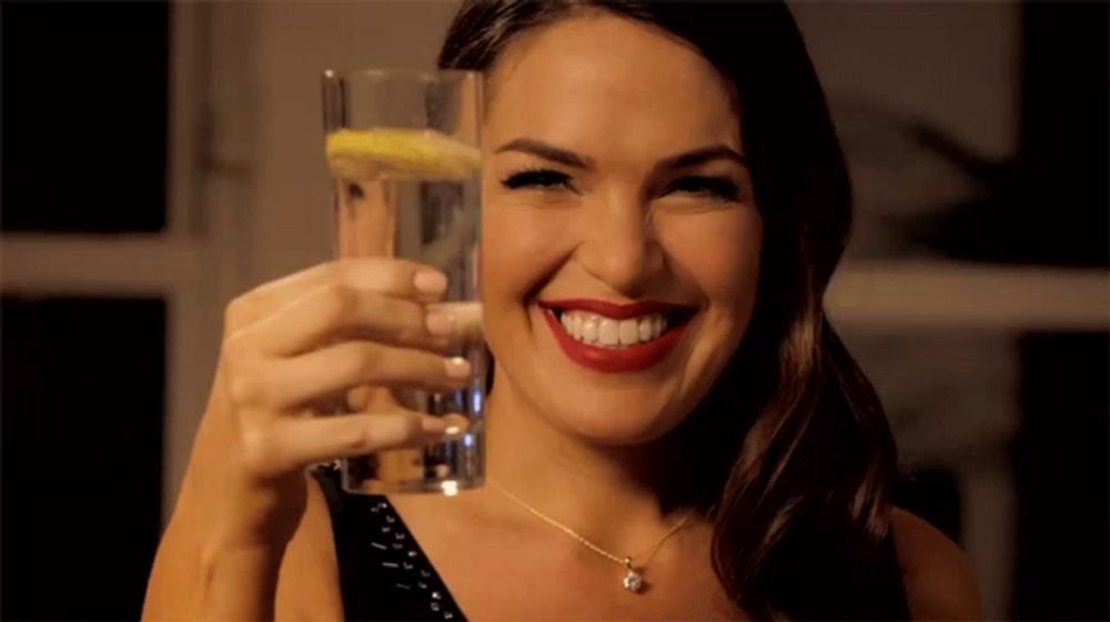 a woman holds up a glass of water with a slice of lemon on it