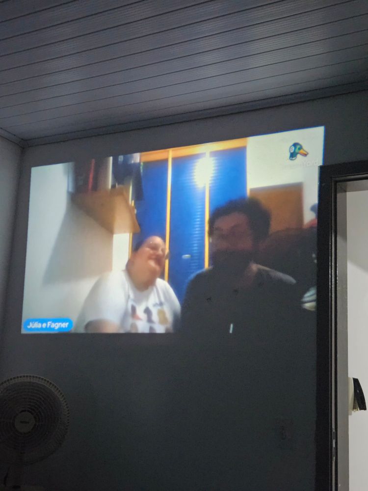 Foto de uma projeção da live no YouTube da Julia Gavilan com ela e o Fagner na tela