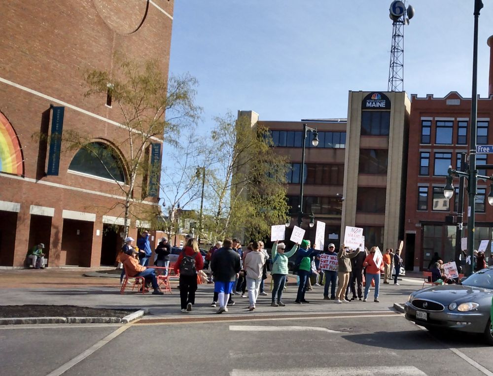 People gathering at a city square in front of an art museum, with a TV station building across the street.