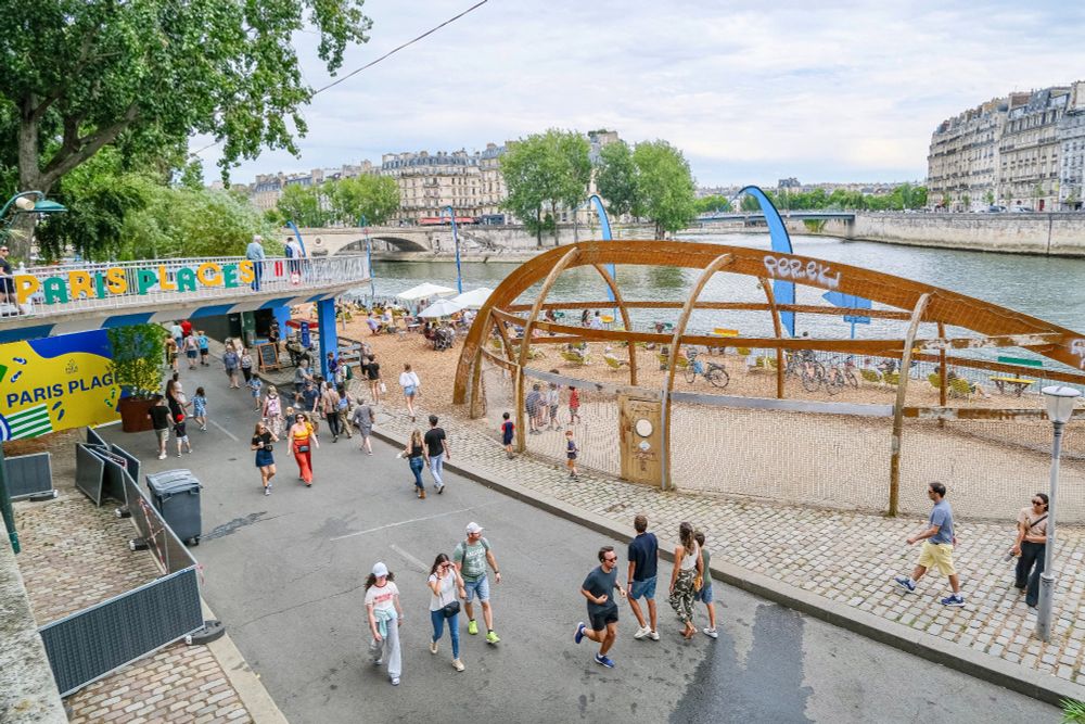 People in casual summer attire walk, cycle, lounge, drink and dine on the “Paris Plages”, a temporary artificial beach installed along the River Seine each summer.