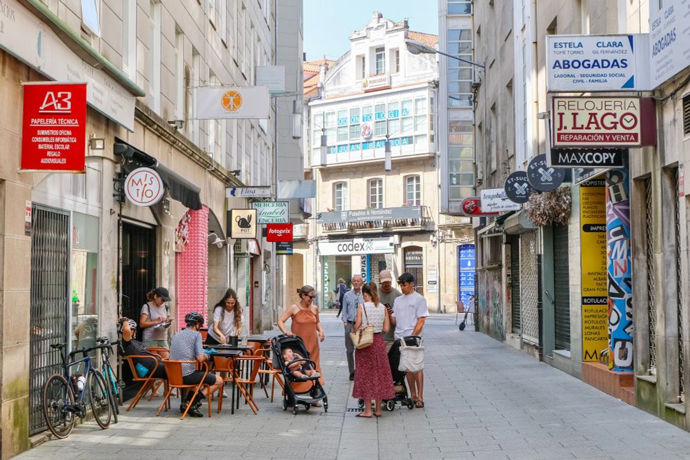 People of all ages and abilities walk, cycle, sit, and socialise on the car-free streets of Pontevedra, which are lined with buildings, trees, benches, and patios.