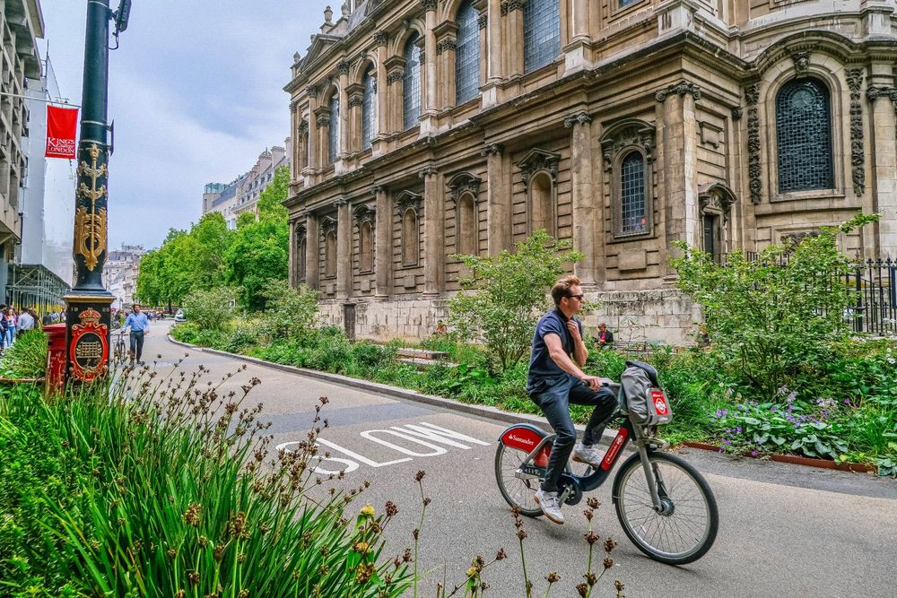 People of all ages and abilities walk, cycle, sit, and socialise on the Strand Aldwych—a former arterial turned pedestrian zone in London, which is lined with buildings, trees, flowers and plantings, benches, and terraces.