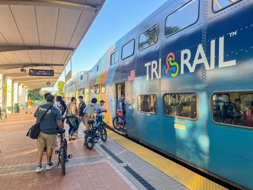 Passengers wait with their bicycles to board a blue commuter train on a platform in Fort Lauderdale, Florida.
