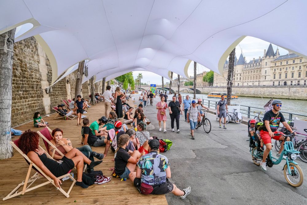 People in casual summer attire walk, cycle, lounge, drink and dine on the “Paris Plages”, a temporary artificial beach installed along the River Seine each summer.