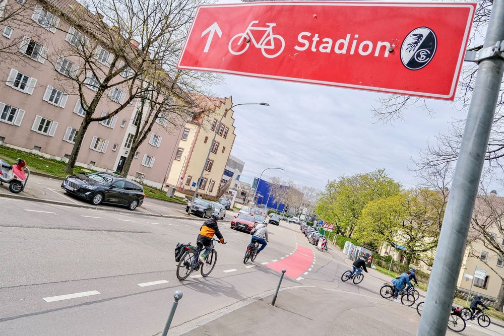 Six cyclists ride in a bike lane past a red sign reads "Stadion" with a bike symbol in Freiburg, Germany.