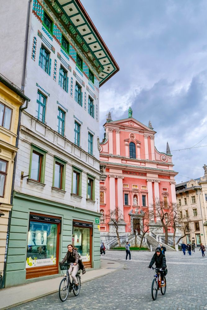 Cyclists and pedestrians navigate a car free street lined with colorful and ornate buildings in the historic center of Ljubljana.