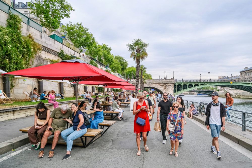 People in casual summer attire walk, cycle, lounge, drink and dine on the “Paris Plages”, a temporary artificial beach installed along the River Seine each summer.
