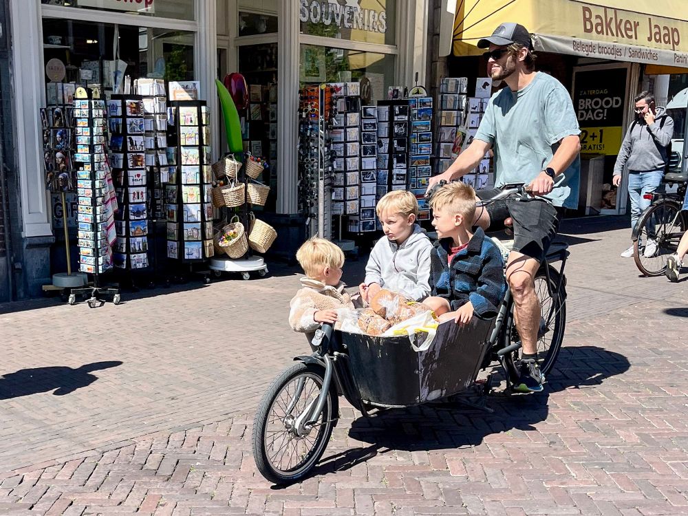 People of all ages and abilities in casual spring attire ride bicycles along dedicated infrastructure on the streets of Delft.