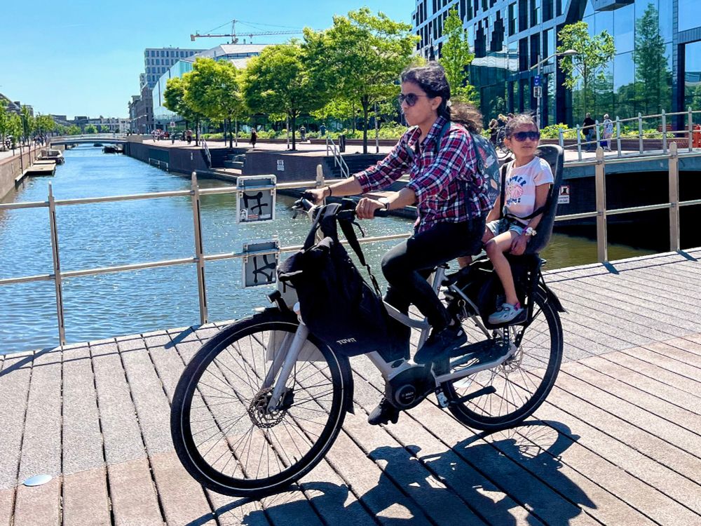 People of all ages and abilities in casual spring attire ride bicycles along dedicated infrastructure on the streets of Delft.