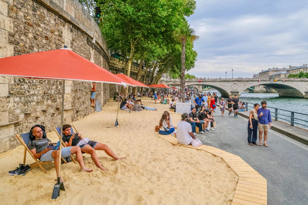 People in casual summer attire walk, cycle, lounge, drink and dine on the “Paris Plages”, a temporary artificial beach installed along the River Seine each summer.