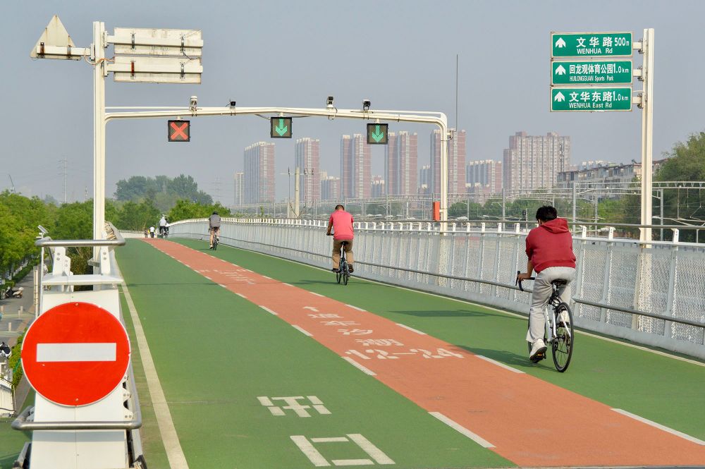 People of all ages and abilities ride bicycles along a green- and orange coloured dedicated and elevated cycle path in Beijing.