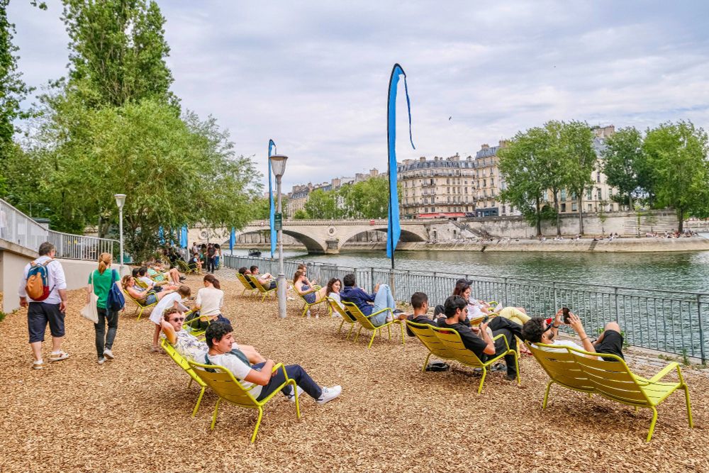 People in casual summer attire walk, cycle, lounge, drink and dine on the “Paris Plages”, an artificial beach installed along the River Seine each summer.